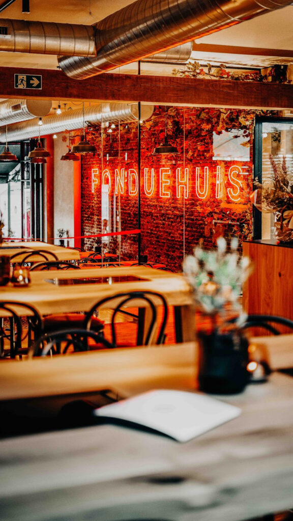 Restaurant interieur met rode 'FONDUEHUIS' neon verlichting en een bakstenen muur.