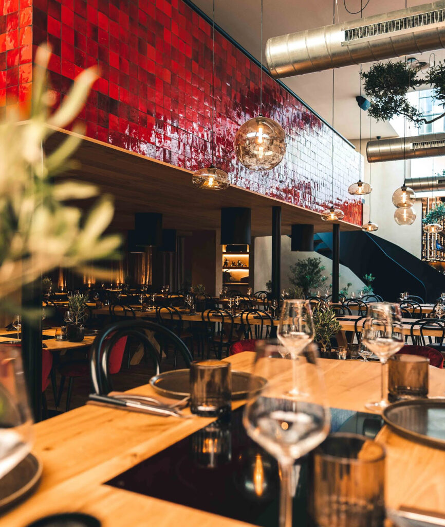 Stijlvol fondue restaurant met een opvallende rode betegelde muur, hangende globe lampen en een sfeervol gedekte tafels.