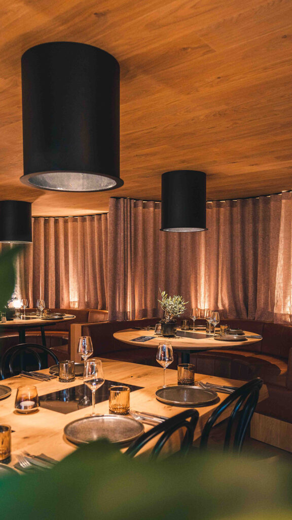 Intiem en stijlvol restaurantgedeelte met houten wanden, ronde banken en grote zwarte hanglampen, klaar voor een comfortabele eetervaring.