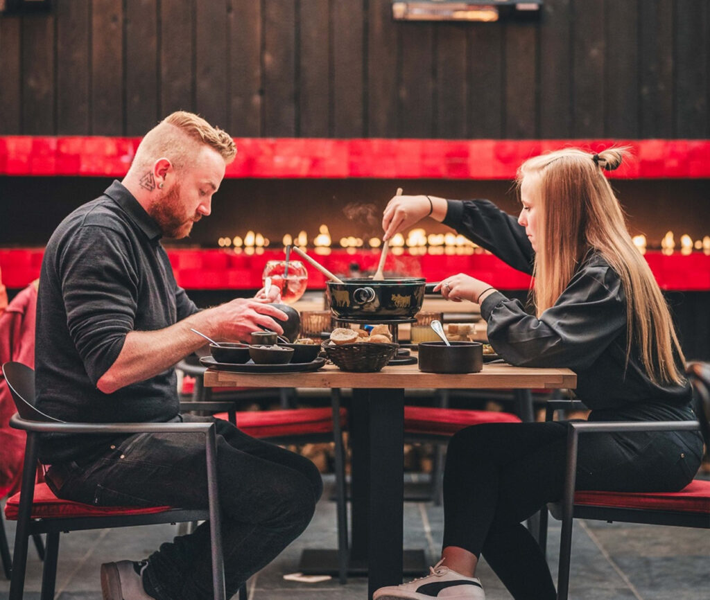 Vrienden genieten van een fondue maaltijd in een sfeervol ingericht restaurant met moderne hanglampen en zwarte en rode decoraccenten.